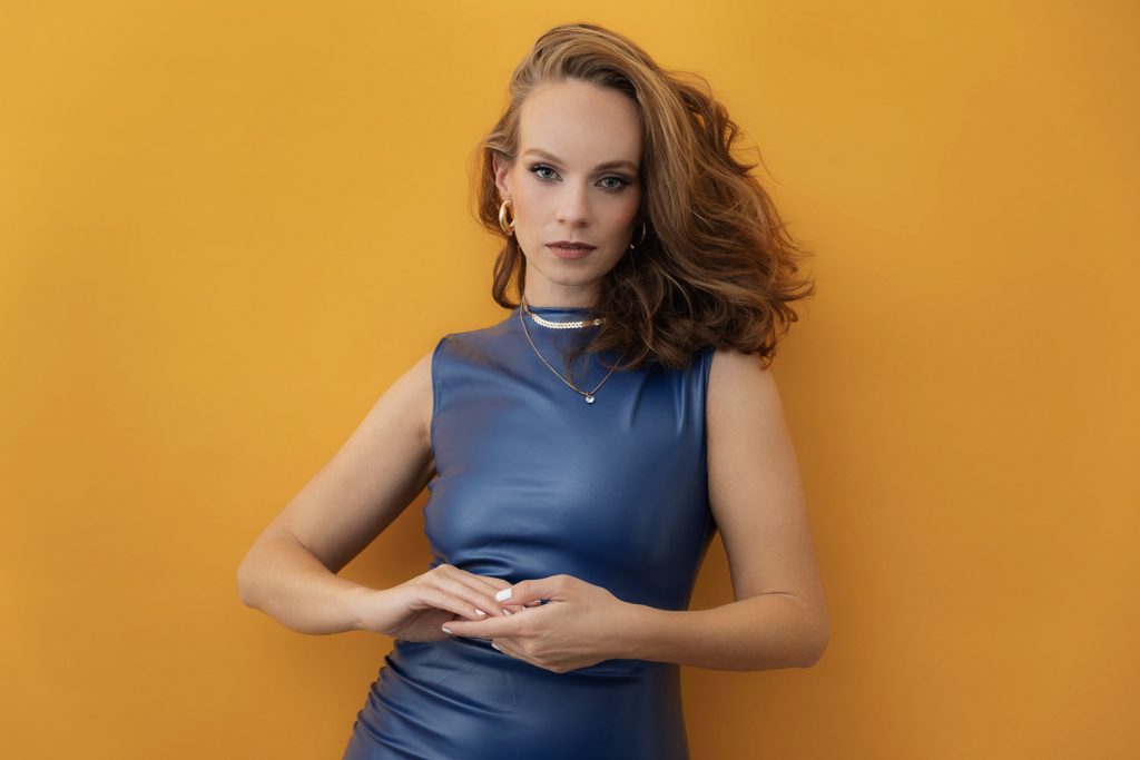 Professionelles Portrait einer Frau im Studio mit orangefarbenem Hintergrund und blauem Kleid, Modefotografie Fotograf München